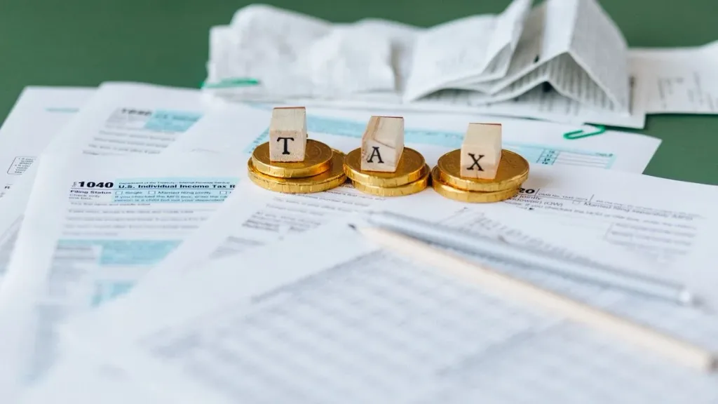 Tax documents and gold coins arranged on a green desk with a calculator