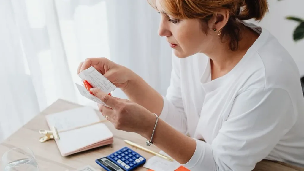 Woman counting money while using a laptop at a desk