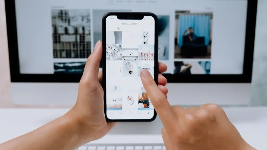 Hands holding a smartphone with a desktop computer nearby